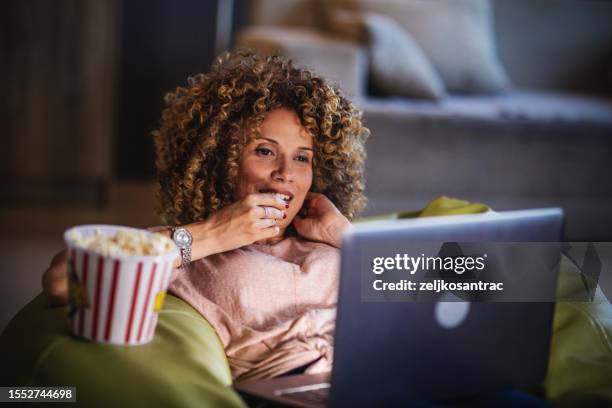 single woman watching online tv and lying on a bad in the living room - downloading stock pictures, royalty-free photos & images