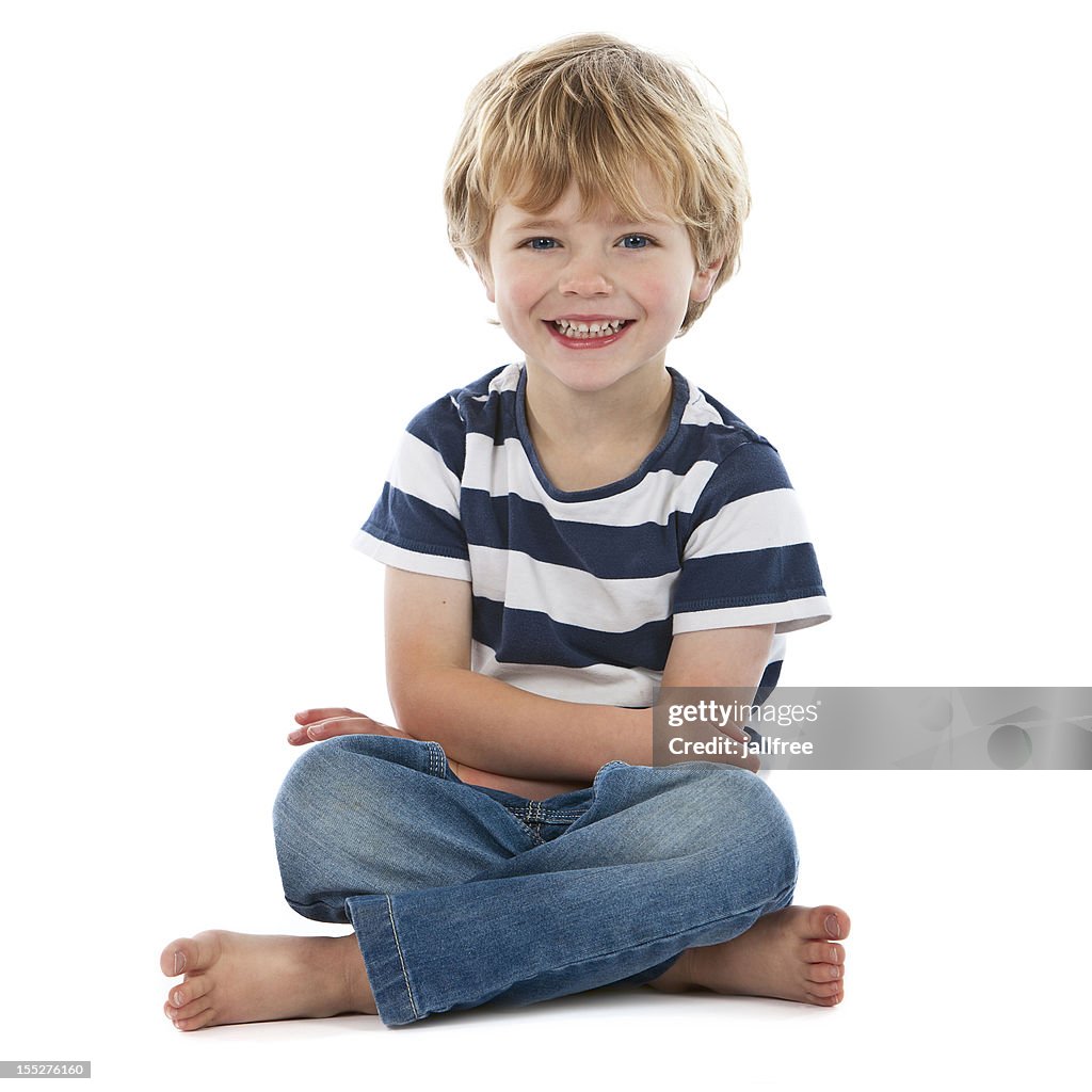 Small boy sitting crossed legged smiling on white