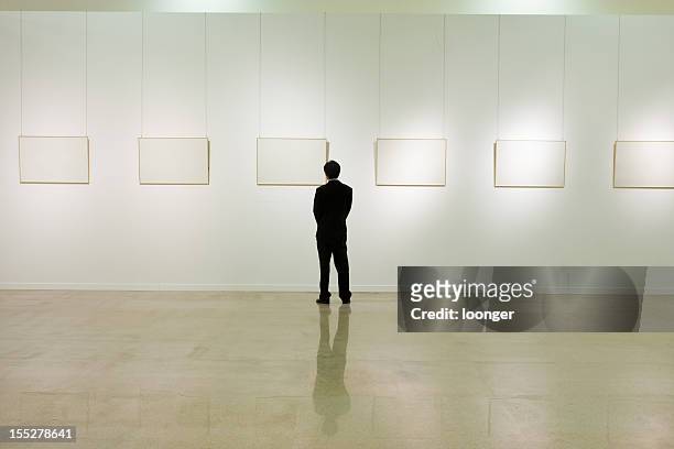 businessman looking at white frames in an art gallery - art gallery back stock pictures, royalty-free photos & images