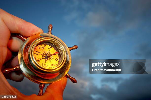 one hand holding a compass and a cloudy sky - rudder stock pictures, royalty-free photos & images