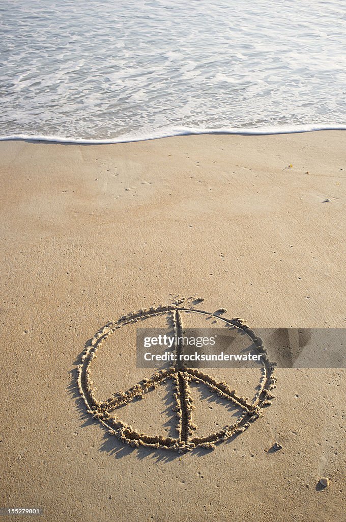 Peace symbol drawn in beach sand near ocean's edge