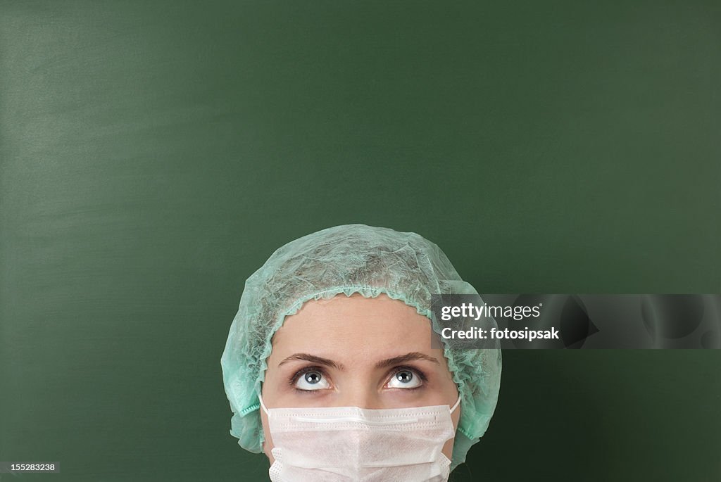 Woman in mask and hair net in front of green chalkboard