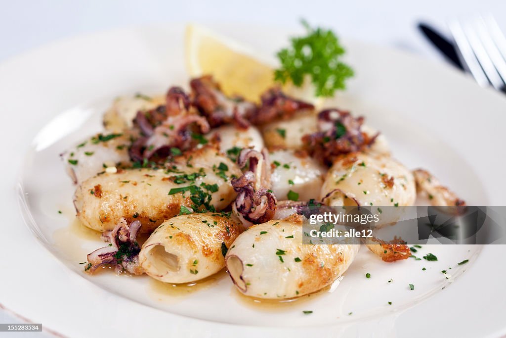 A plate of seafood entree with squid on top