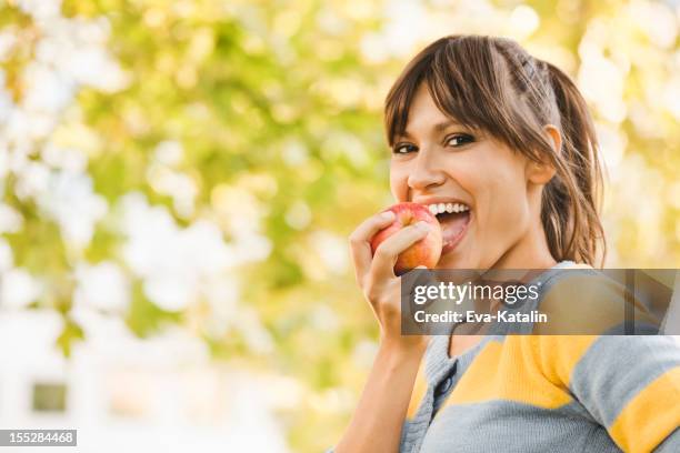 fröhliche junge frau essen einen apfel - biting on something stock-fotos und bilder