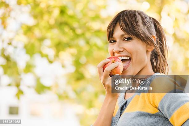 alegre joven mujer comiendo una manzana - manzana fotografías e imágenes de stock