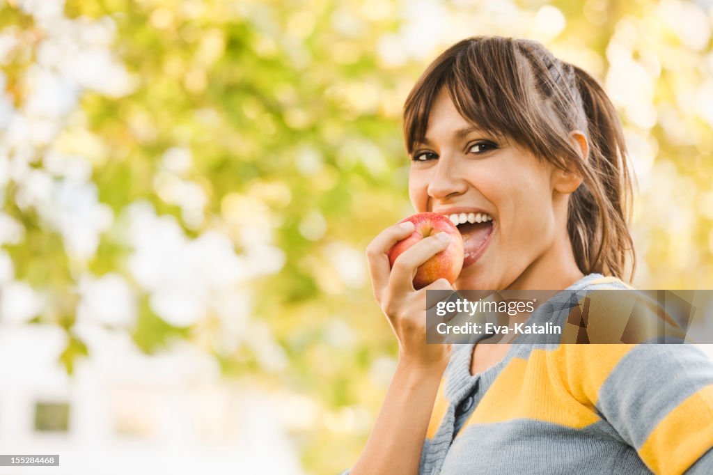 Cheerful young woman eating an apple