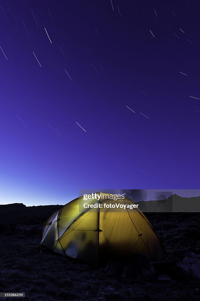 Star trails over yellow mountain tent