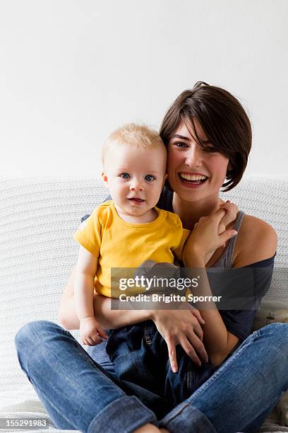 mother and baby sitting on bed - mom sits on sons lap stock-fotos und bilder