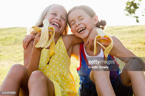 laughing girls eating bananas outdoors - child eating a fruit stockfoto's en -beelden