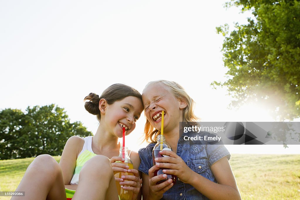Laughing girls drinking juice outdoors