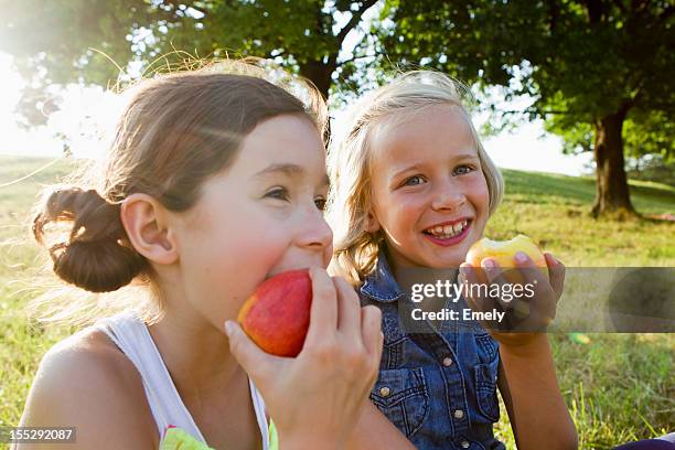 laughing girls eating apples outdoors - child eating a fruit stockfoto's en -beelden