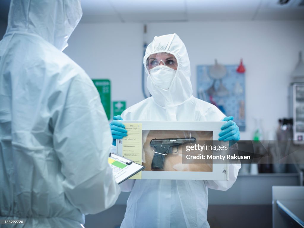 Forensic scientist holding evidence box containing gun from crime scene