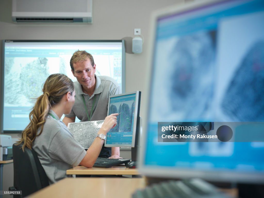Trainee forensic scientists examining fingerprints on screens in laboratory