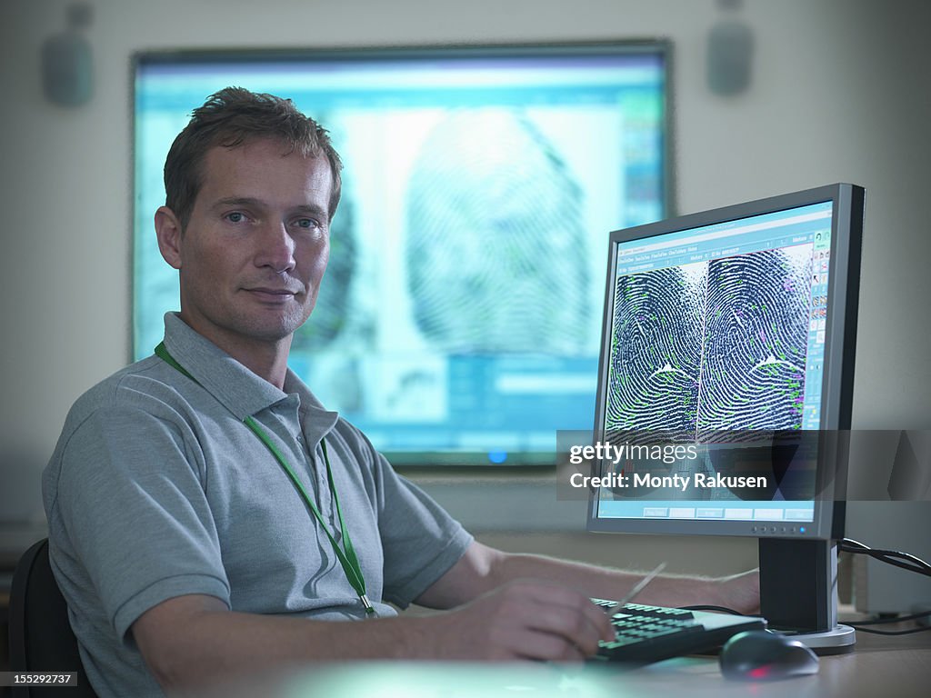 Portrait of forensic scientist at desk with fingerprints on screen in laboratory