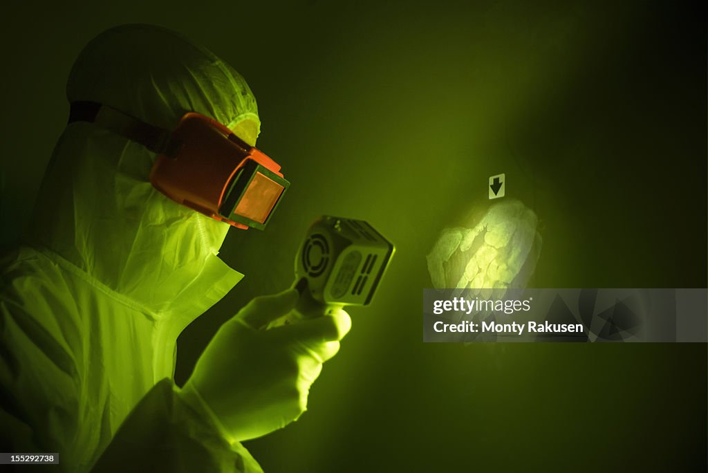 Forensic scientist using finger print light to find hand print on wall at crime scene