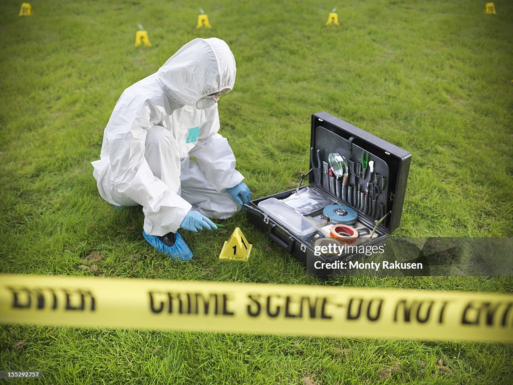 Forensic scientist inspecting toolkit at crime scene, police tape in foreground