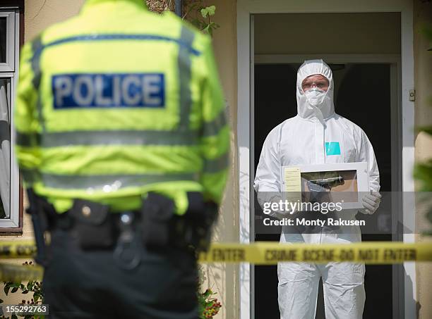 forensic scientist holding evidence box containing firearm at crime scene, policeman in foreground - uk police officer stock pictures, royalty-free photos & images