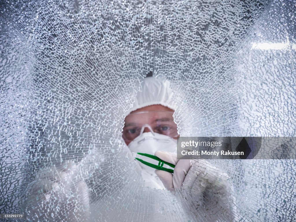 Forensic scientist removing fragment of broken glass with tweezers at crime scene