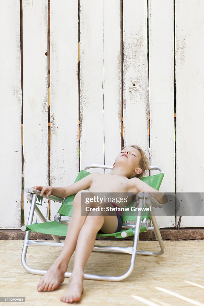 Boy in swimsuit in lawn chair indoors
