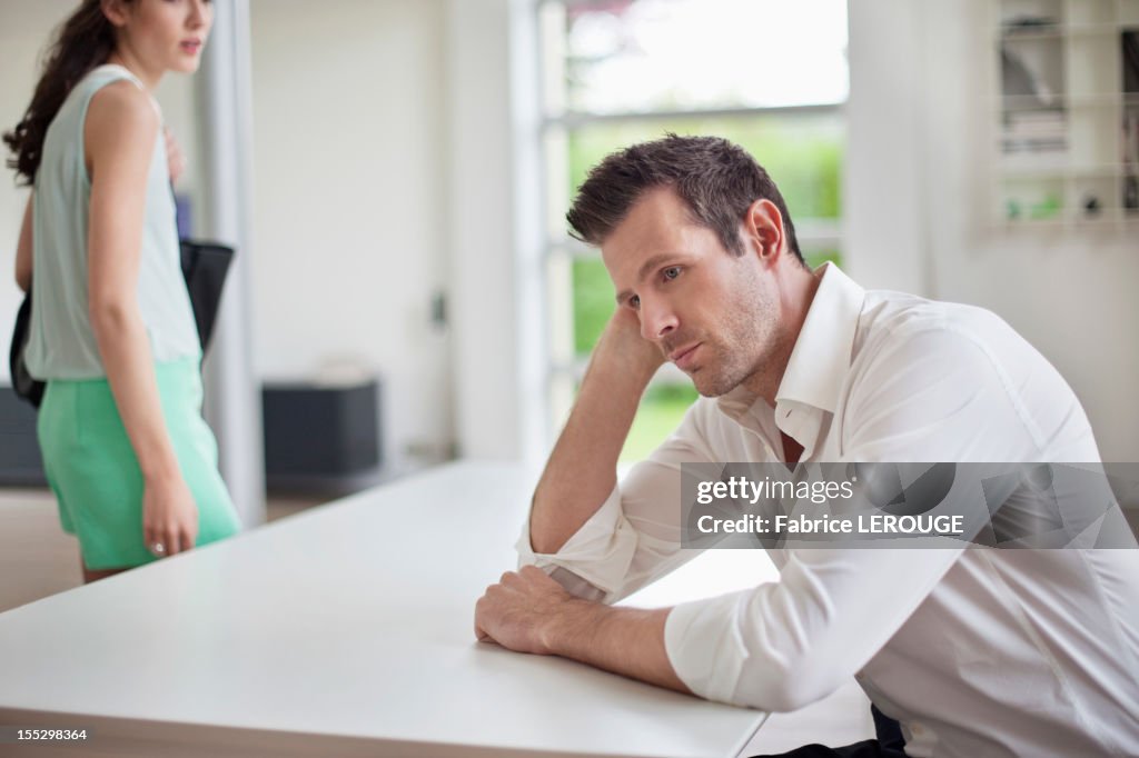 Man sitting at a table with a woman leaving the home