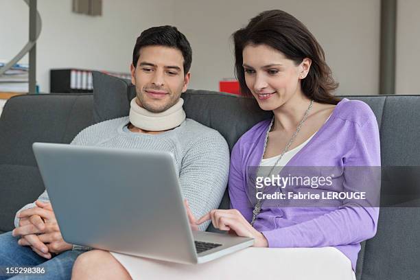 woman using a laptop with her husband beside her - collarín médico fotografías e imágenes de stock