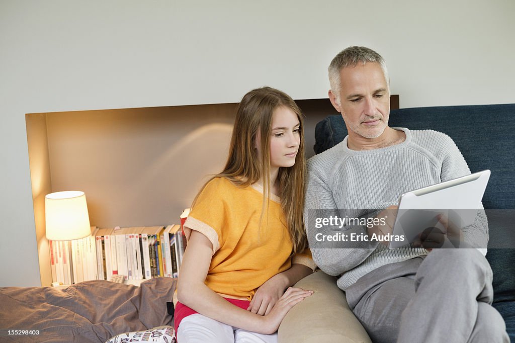 Man using a digital tablet with his daughter at home