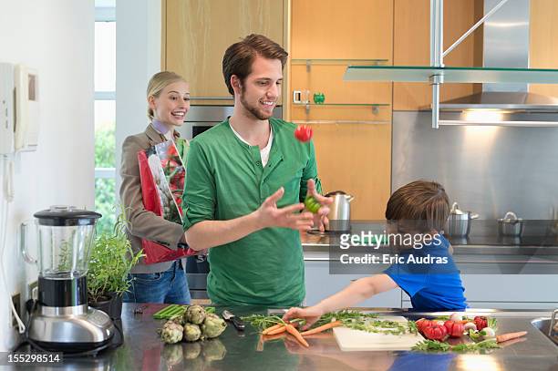parents looking at their son cutting vegetables in the kitchen - throwing tomatoes stock pictures, royalty-free photos & images