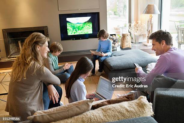 family using electronic gadgets in a living room - tv phone tablet stock-fotos und bilder