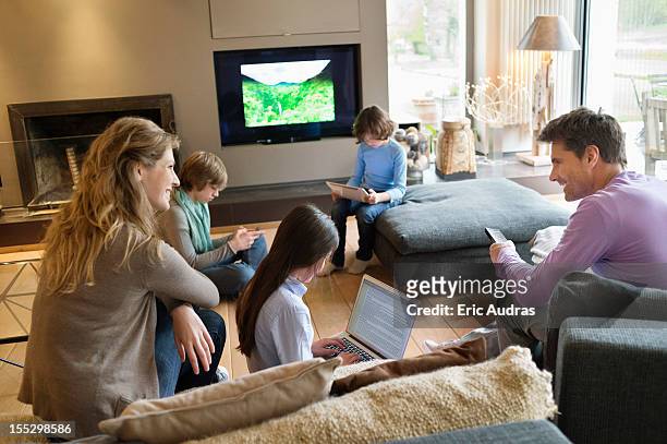 family using electronic gadgets in a living room - tv phone tablet stock pictures, royalty-free photos & images