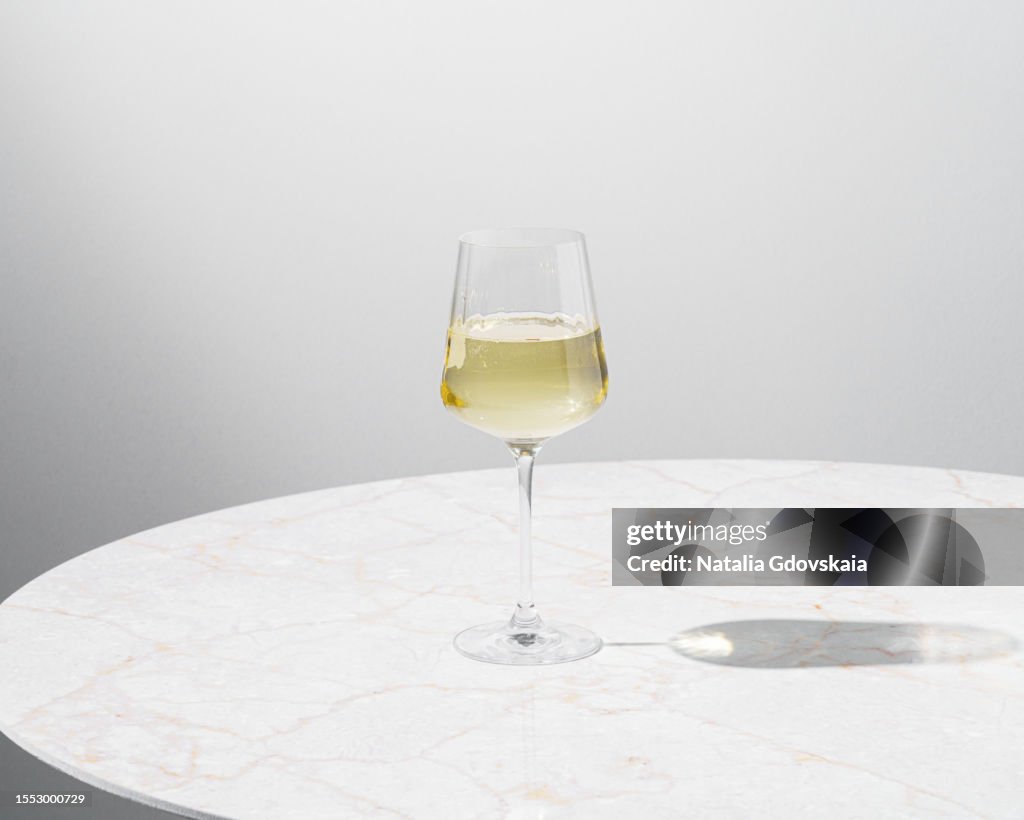 Round coffee table with glass of white wine. Table is in sunny spot, hard shadows from sun.