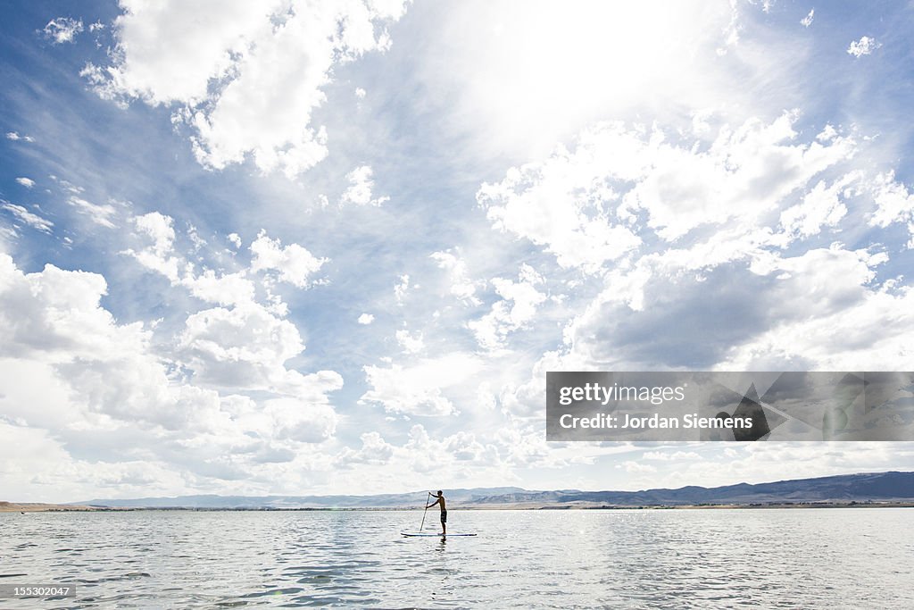 A male enjoys a stand up paddle board.