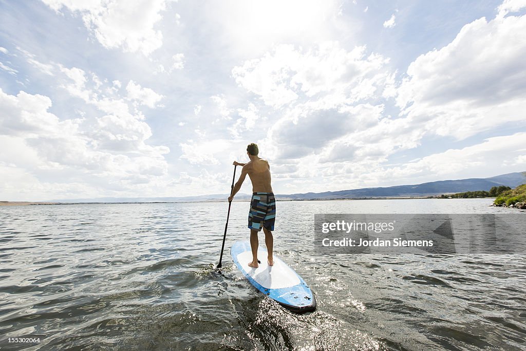 A male enjoys a stand up paddle board.