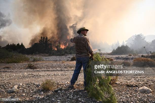Local man holds a pine tree branch to beat down the approaching wildfires burn in the background, near the village of Vati, just north of the coastal...