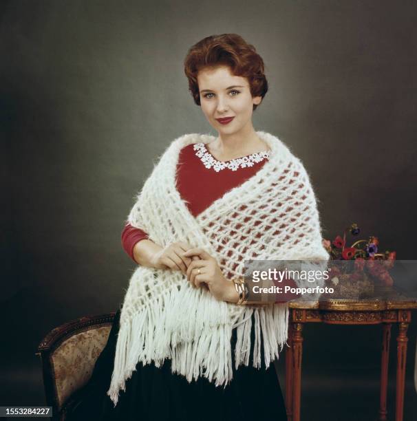 Posed studio portrait of a female fashion model wearing a white fringed mohair shawl over a red sweater with white decoration around the neck,...