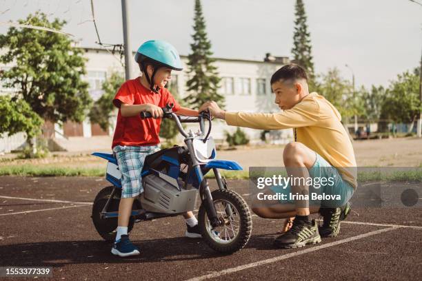 ein kleiner junge mit schutzhelm sitzt auf einem elektrofahrrad. der instruktor bringt dem kind bei, an sonnigen sommertagen im freien ein elektromotorrad zu fahren. freizeitaktivitäten für kinder. - baby sturzhelm stock-fotos und bilder