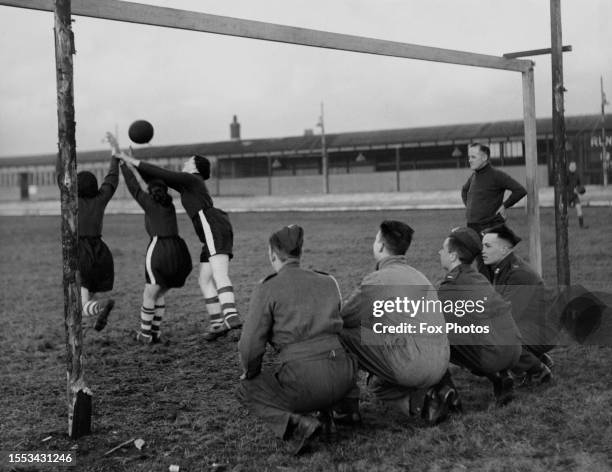 Soldiers squat directly behind the goal, watching players of Bolton Women's football club during a training session at their ground in Raikes Park in...