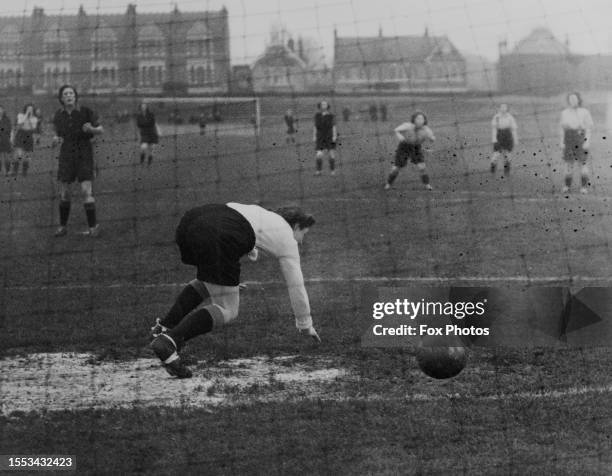 The diving goalkeeper fails to stop the shot during a women's football match, with the teams wearing strips comprising dark shirts and dark shorts,...