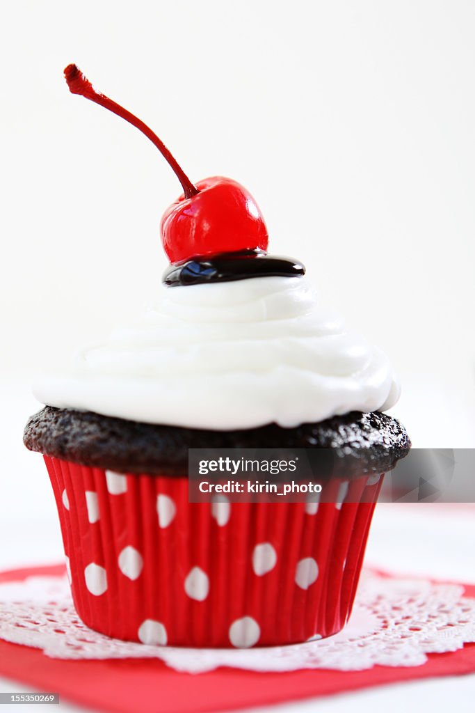 A retro styled chocolate cupcake with white icing and cherry