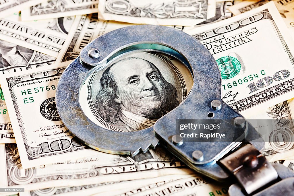 Handcuffs circle Benjamin Franklin in stack of dollars