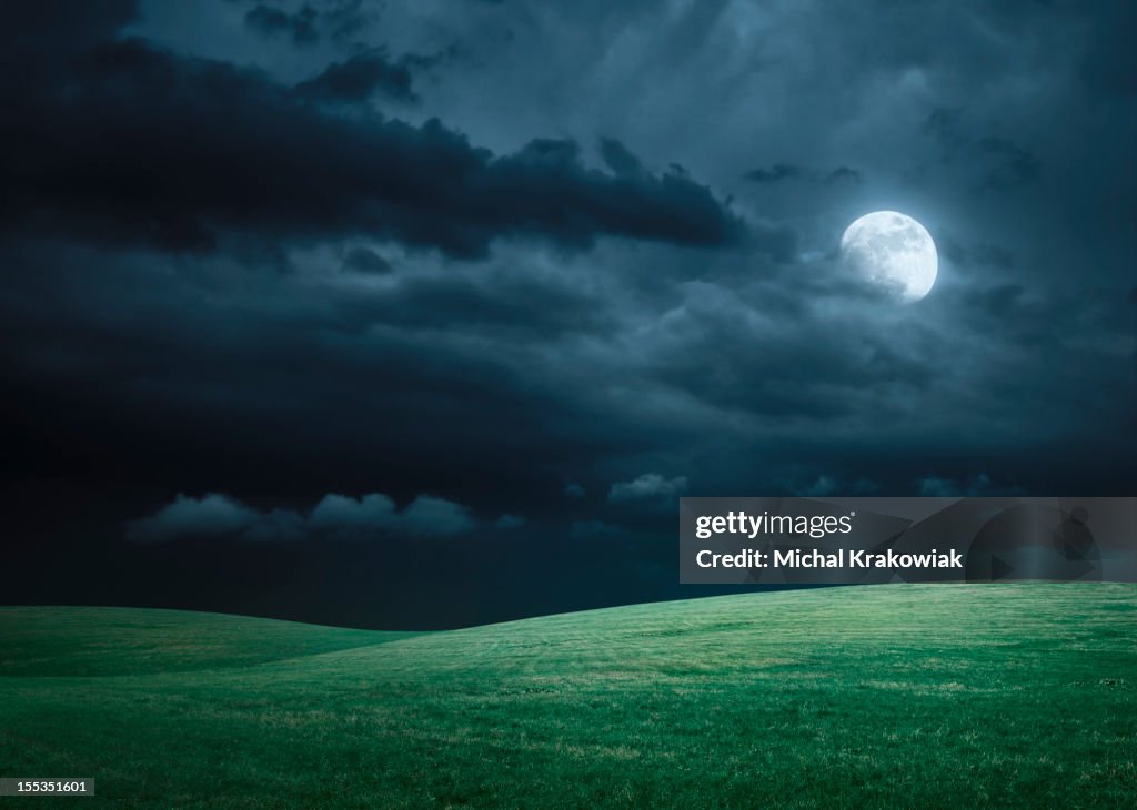 Hilly meadow at night with full moon, clouds and grass