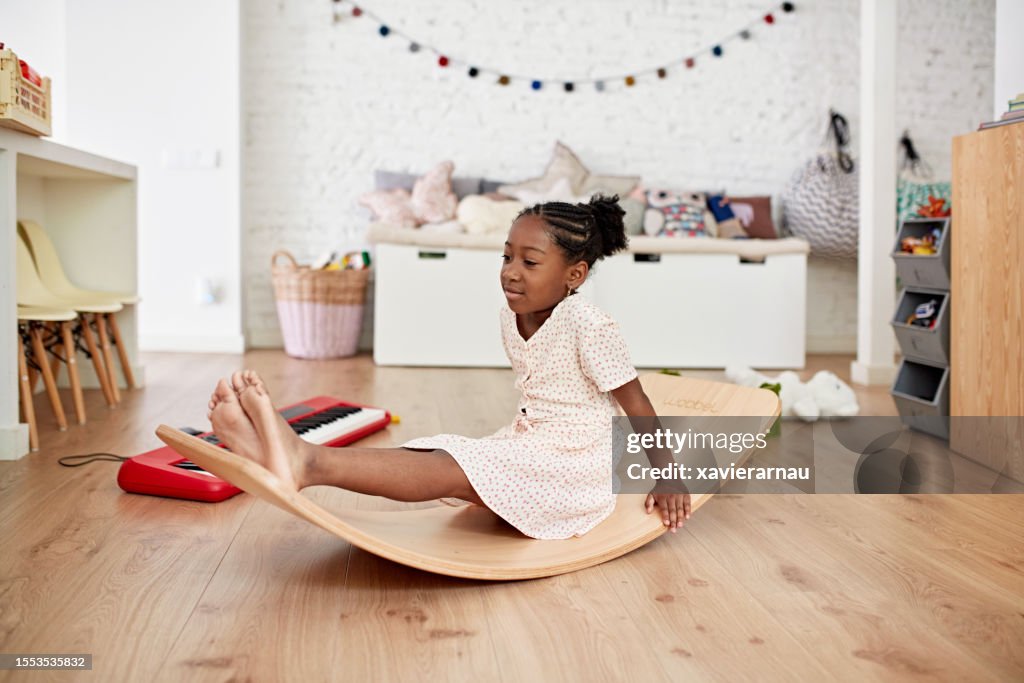 Menina negra sentada na prancha de equilíbrio