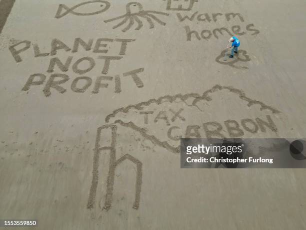 People write their own messages in the sand next to a giant sand drawing entitled 'Postcards from the Edge' sending a message to UK Prime Minster...
