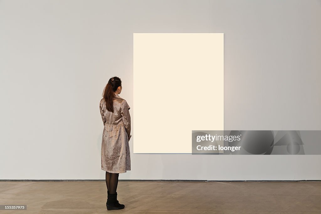 One woman looking at white frame in an art gallery