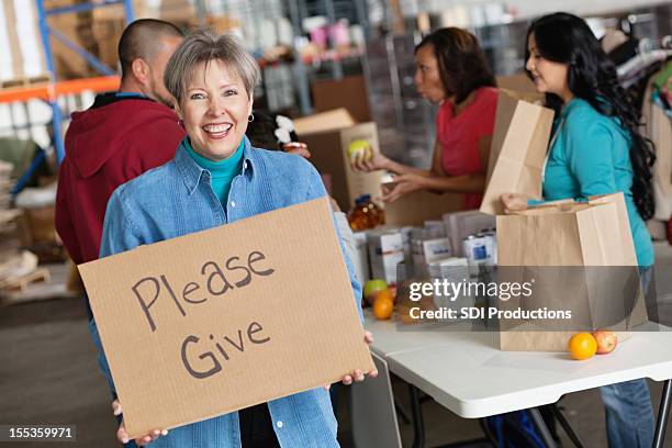 mature woman promoting giving with a sign at donation center - pleading stock pictures, royalty-free photos & images