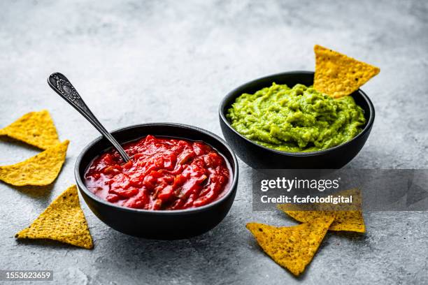 bowls of salsa sauce and guacamole with nacho chips on gray background - guacamole 個照片及圖片檔