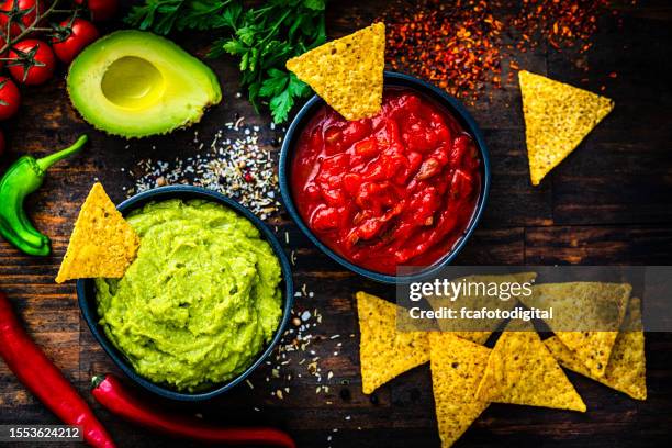 mexican food: salsa sauce, guacamole and nacho chips shot from above on dark wooden table. - tex mex food stock pictures, royalty-free photos & images
