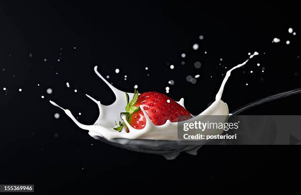 strawberry splashing into spoon full of milk - strawberries and cream stockfoto's en -beelden