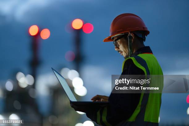 boosting key front-line operations through digitization to driving sustainability in oil and gas industry. side view of engineer working over a laptop computer to analyze insights related to the production of energy in field operation. - oil refinery stock pictures, royalty-free photos & images