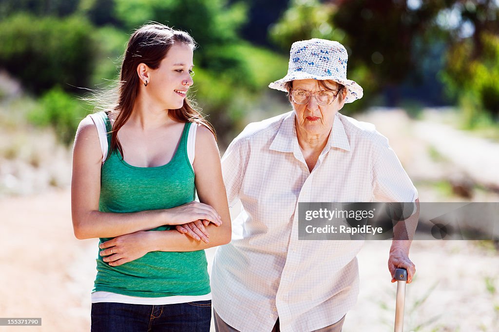 Young woman helping old lady with stick to walk