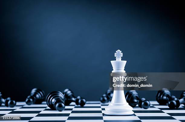 white chess king among lying down black pawns on chessboard - rivalry stock pictures, royalty-free photos & images